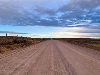 Dirt road amidst field against sky