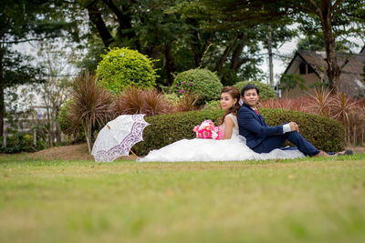 Portrait of friends sitting on grass against trees