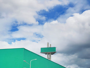 Green empty advertisement billboard on large green warehouse against blue cloudy sky