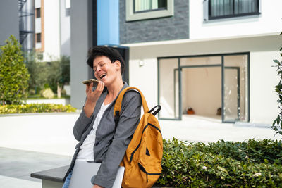 Young woman looking away while standing against building