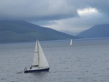 Sailboat sailing on sea against mountains