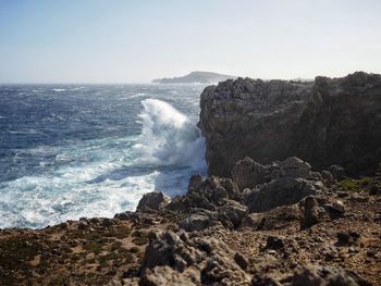 Waves breaking on rocks at shore against sky