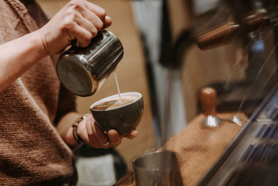 Midsection of barista pouring coffee in cup