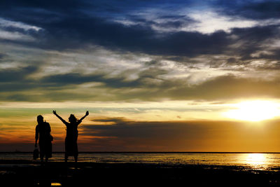 Silhouette people standing on beach against sky during sunset