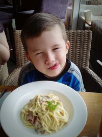 Cute boy sticking out tongue while having noodles at restaurant