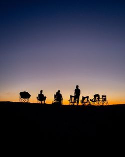 Silhouette people and camp chairs against clear sky during sunset