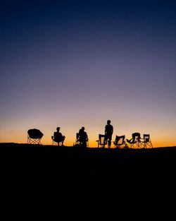 Silhouette people at beach against clear sky during sunset