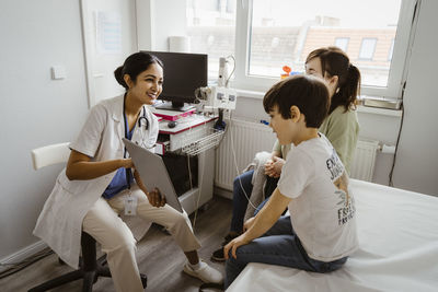 Female pediatrician discussing with mother and son over tablet pc in examination room at clinic