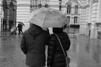 Rear view of people holding umbrella while standing on street during rainy season