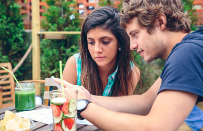 Friends using mobile phone by food and drink at restaurant