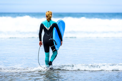 Rear view of woman with surfboard walking at beach