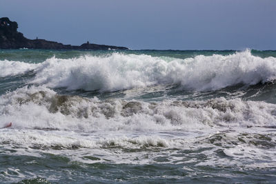 Waves splashing on shore against clear sky