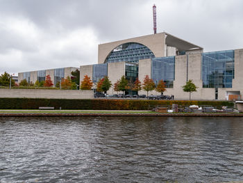 Buildings by river against cloudy sky