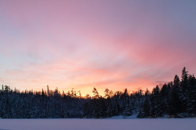 Snow covered land against sky during sunset