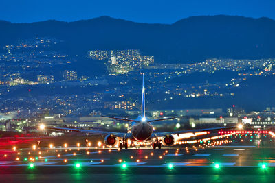 Airplane landing on runway in illuminated city against sky at night