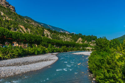 Scenic view of river by mountains against clear blue sky