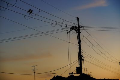 Low angle view of silhouette electricity pylons against sky at sunset