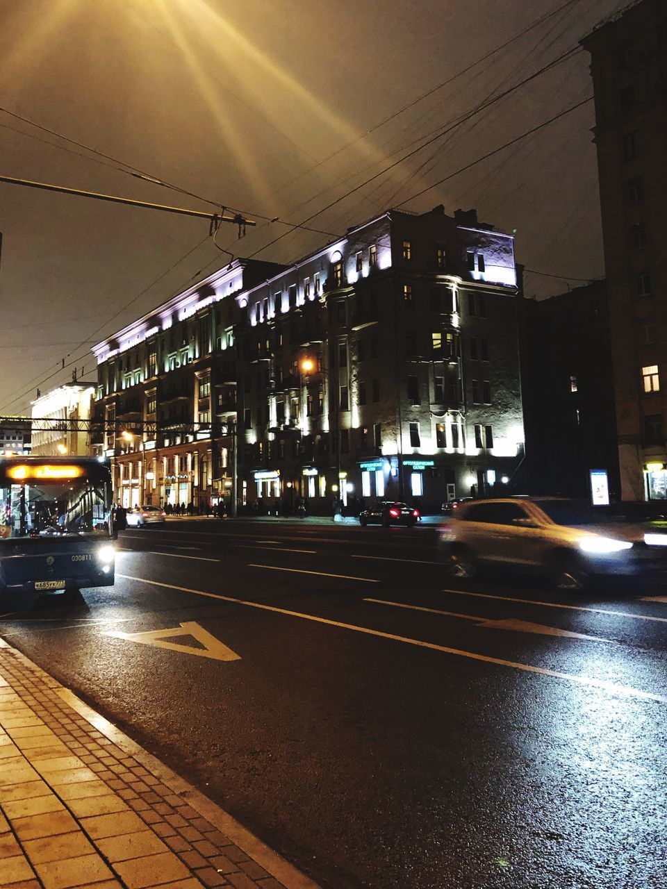 CARS ON ILLUMINATED STREET AMIDST BUILDINGS AT NIGHT