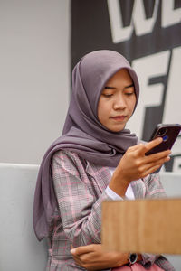 Portrait of asian muslim woman wearing modern hijab sitting and playing social media in cafe