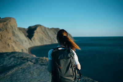 Rear view of woman standing against sea against clear blue sky