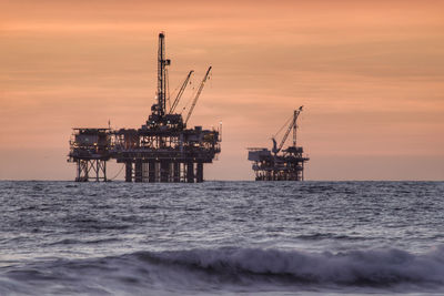 Silhouette crane of oil platform by sea against sky during sunset