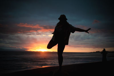 Silhouette woman standing on beach against sky during sunset
