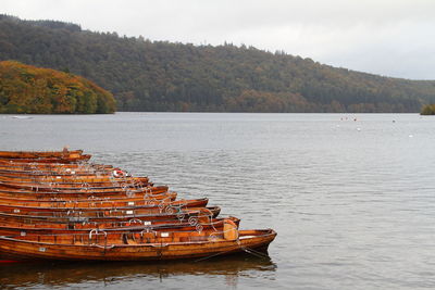 Boats moored by lake against sky