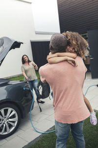 Rear view of man carrying daughter while standing by electric car