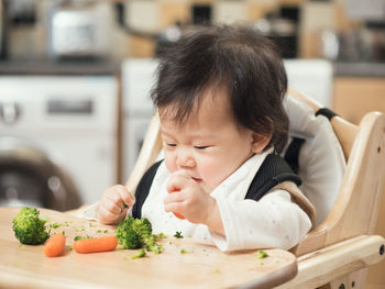 Cute baby girl playing with vegetables on wooden high chair