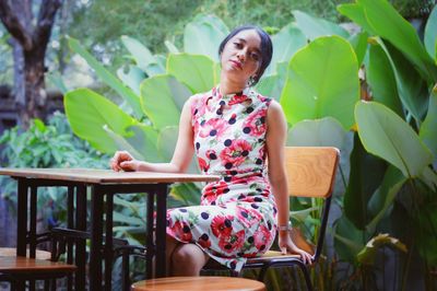 Young woman sitting on chair against trees