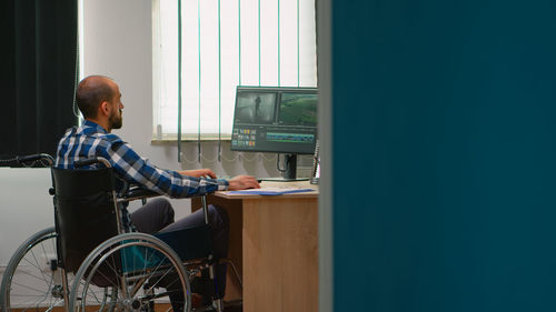 Side view of man using mobile phone while sitting on wheelchair