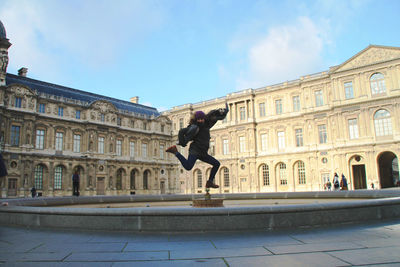 Full length of woman jumping against buildings in city