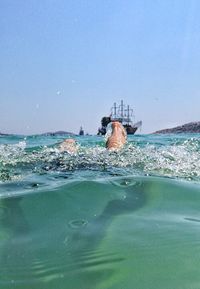 Low section of man swimming in sea against clear sky