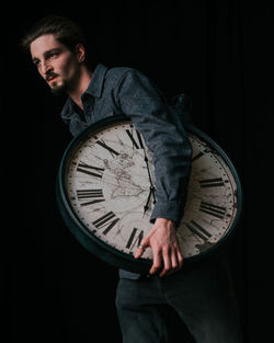Portrait of young man standing against black background