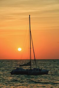 Silhouette boat sailing on sea against orange sky