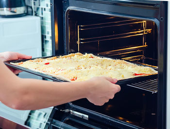 Close-up of person putting pizza into oven