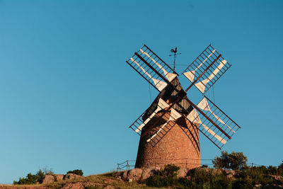 Low angle view of traditional windmill on field against clear blue sky