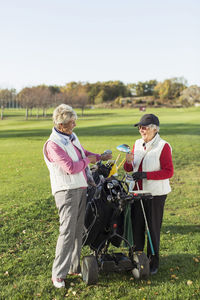 Full length of smiling senior women with golf bag on course