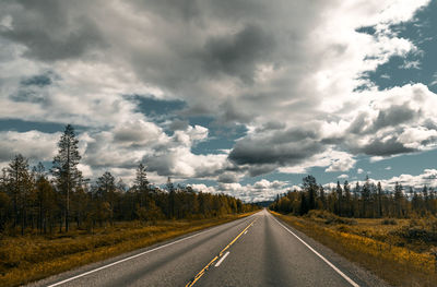 Empty road along trees and against sky