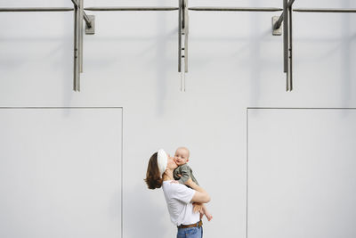 Mother kissing baby boy in front of wall