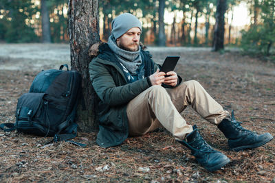 Full length of male hiker using digital tablet while sitting in forest