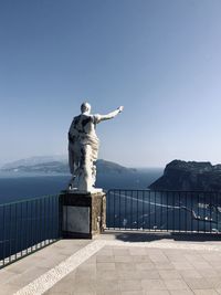 Statue of by sea against clear blue sky