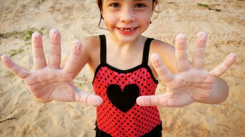 Portrait of girl holding heart shape on sand