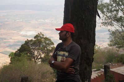 Side view of young man standing against trees