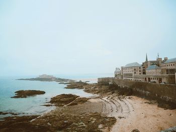 Buildings by sea against clear sky