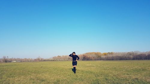 Full length of young woman walking on grassy field against clear blue sky