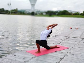 Woman practicing yoga on pier in lake