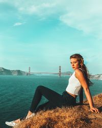 Portrait of teenage girl sitting on shore against sky