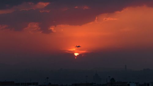 Silhouette airplane flying against orange sky