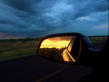 Reflection of car on side-view mirror against sunset sky